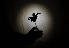 Chinese shadow theater for children projected on a bed sheet, themed of Saint George, April 23. The shadows are of cardboard with a little basset, you can also see the hand that manipulates them. tales, the fairy, storyteller.
