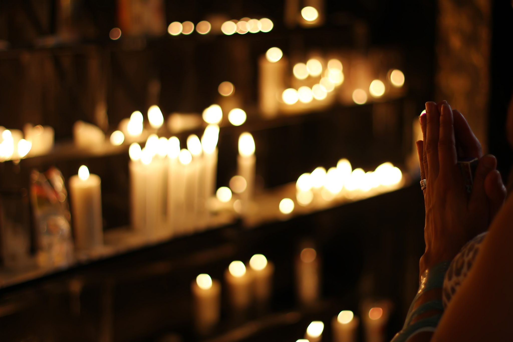 close-up-photograph-of-person-praying-in-front-lined-candles-1024900